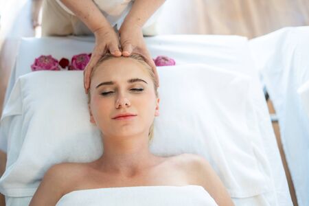 Beautiful blonde girl is lying with closed eyes at spa while a massage therapist is massaging her...
