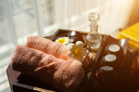 Spa accessories wellness setting with pink pastel towel, cosmetic bottles, aroma oil, white plumeria flower in tray, massage stones in wooden bowl and spa candle, spa concept, copy spaceの写真素材