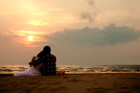 Couple in love watching sunset together on beach travel summer holiday. Silhouette bride and groom with bouquet enjoy view sunset sea on tropical destination vacation. Romantic couple on the beachの写真素材