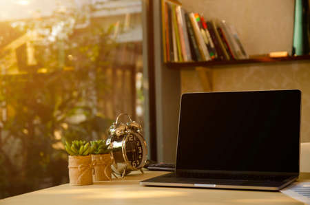 Work desk in home office  laptop/notebook computer, clock, calculator, report paper, cactus tree and cup of coffee in morning. Work hours & lifestyle business. Work from homeの写真素材