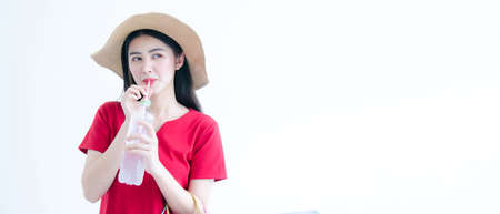 Portrait of happy young asian woman in red dress and knit hat drinking water while holding shopping bags isolated over white backgroundの写真素材