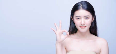 Beauty portrait of cheerful attractive half naked asian woman with smiling face showing ok gesture sign and looking forward at camera isolated bright blue background. Expressive facial expressionsの写真素材