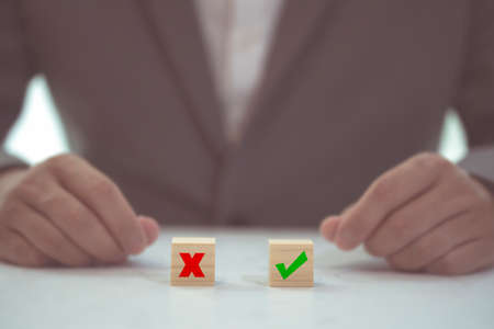 Business decision concept. Businessman manager confuse to make decision with project between approve or reject. Hand arranging symbol with icon on wood cube block. Solution to success projectの写真素材