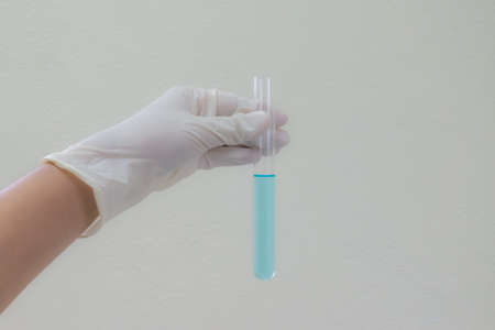 Color liquid in test tube hold in left hand with glove of scientist isolated on the light plain wall