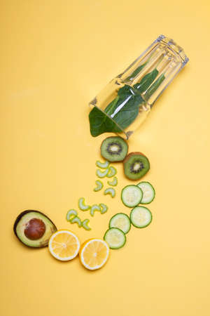 glass with green fruit falling and yellow backgroundの写真素材