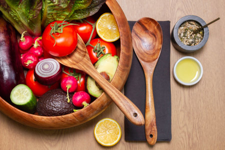 Wooden salad bowl and servers with all the row ingredients with black napkins and some oil with seed mixedの写真素材
