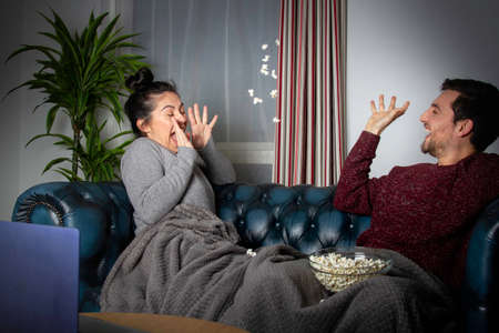 couple sitting on the sofa playing with popcornの写真素材