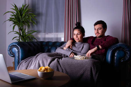a couple watching a film on the sofa eating pop cornsの写真素材