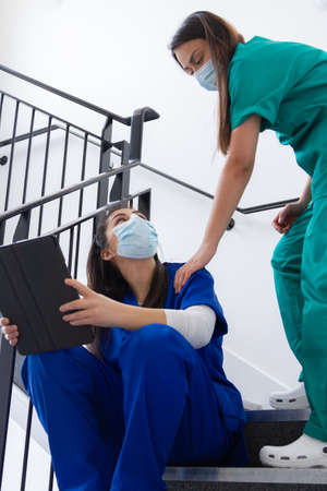 doctor sitting on the stairs with a tablet and other doctor passing down the stairsの写真素材