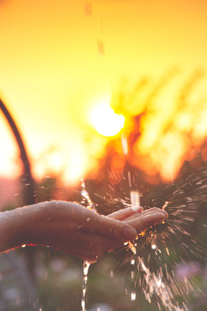 a hand taken water drops with the sun on the backgroundの写真素材