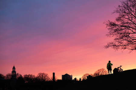 unrecognizable man taking a photo on the hill with his phone with a colorful skyの写真素材