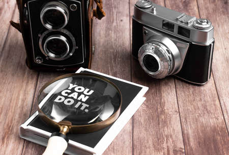two cameras and magnifying glass are on wooden table with a bookの写真素材