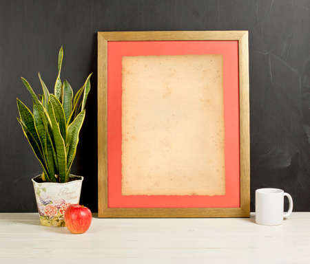 Mock up of blank photo frame with plant pot, mug and apple on wooden shelfの写真素材