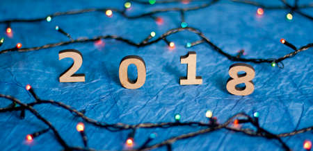 Wooden numbers forming the number 2018 and Christmas lights on a blue paper backgroundの写真素材