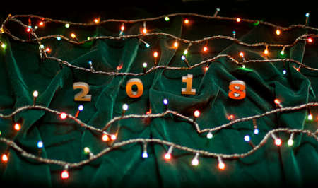 Wooden numbers forming the number 2018 and Christmas lights on a green fabric background