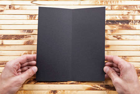 Mens hands holding empty black booklet on bamboo background. View from aboveの写真素材