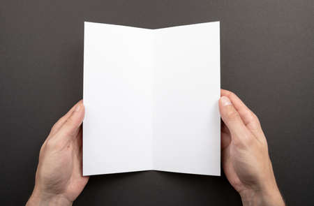 Mens hands holding empty white booklet on gray background. View from aboveの写真素材