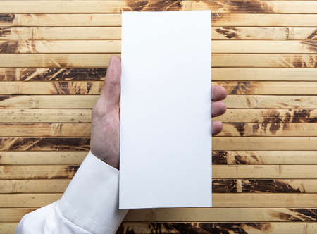 Mens hand holding empty white flyer on bamboo background. Blank paper mock-upの写真素材