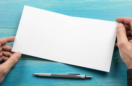 Mens hands holding empty white booklet on blue wooden background. View from aboveの写真素材