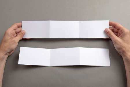 Mens hands holding empty white booklet on gray background. View from aboveの写真素材