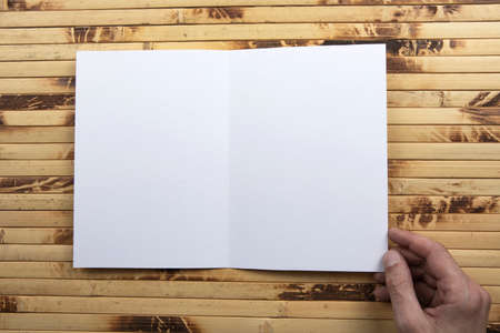 Mens hand holding empty white booklet on bamboo background. View from above