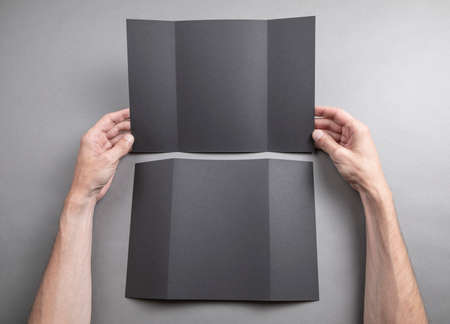 Mens hands holding empty black booklet on gray background. View from above