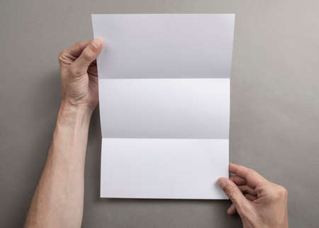 Mens hands holding empty white booklet on gray background. View from above
