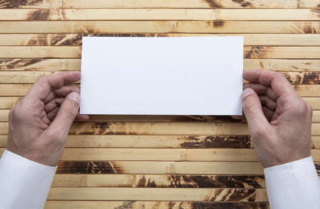 Mens hands holding empty white flyer on bamboo background. Blank paper mock-up