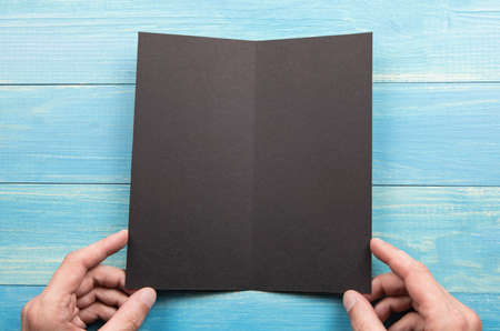 Mens hands holding empty black booklet on blue wooden background. View from aboveの写真素材