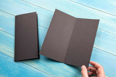 Mens hand holding empty black booklet on blue wooden background. View from aboveの写真素材