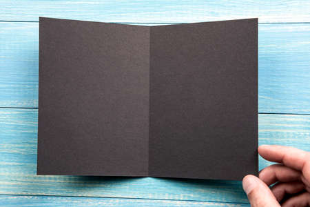 Mens hand holding empty black booklet on blue wooden background. View from aboveの写真素材