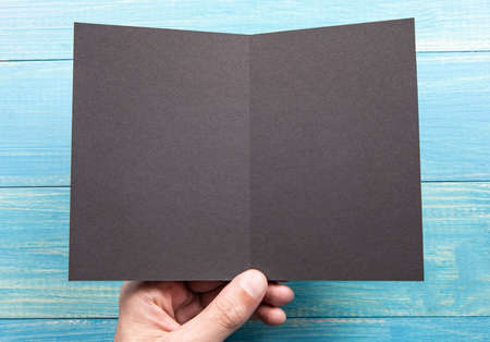 Mens hand holding empty black booklet on blue wooden background. View from aboveの写真素材