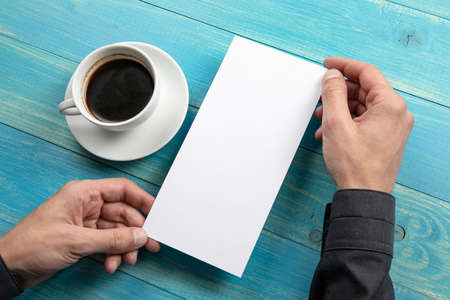 Mens hands holding empty white flyer on blue wooden background. Blank paper mock-upの写真素材
