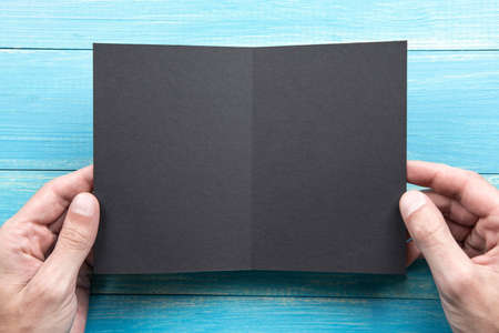 Mens hands holding empty black booklet on blue wooden background. View from aboveの写真素材