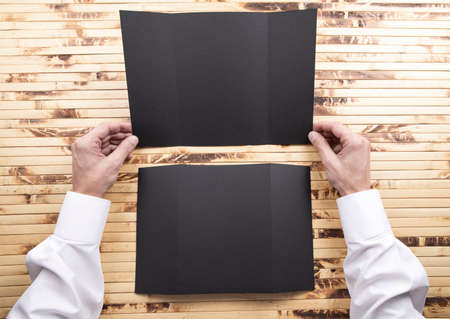 Mens hands holding empty black booklet on bamboo background. View from aboveの写真素材