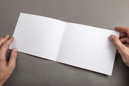 Mens hands holding empty white booklet on gray background. View from above