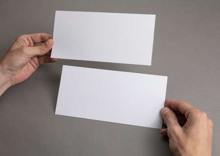 Mens hands holding empty white flyers on light gray background. Blank paper mock-up