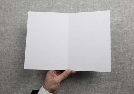 Mens hands holding empty white booklet on gray background. View from aboveの写真素材