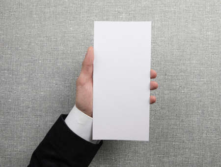 Mens hand holding empty white flyer on light gray background. Blank paper mock-upの写真素材