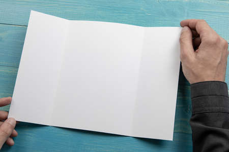 Mens hands holding empty white booklet on blue wooden background. View from aboveの写真素材