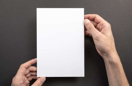 Mens hands holding empty white letterhead on gray background. Blank paper mock-upの写真素材