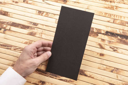 Mens hand holding empty black flyer on bamboo background. Blank paper mock-upの写真素材