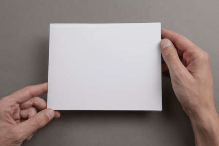 Mens hands holding empty white letterhead on light gray background. Blank paper mock-upの写真素材