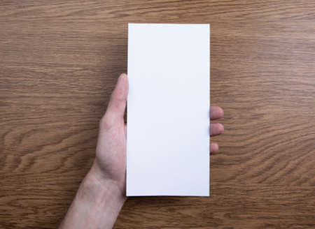 Mens hand holding empty white flyer on wooden background. Blank paper mock-upの写真素材
