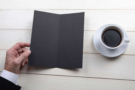 Mens hands holding empty black booklet on gray background. View from above