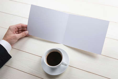 Mens hands holding empty white booklet on wooden background. View from aboveの写真素材