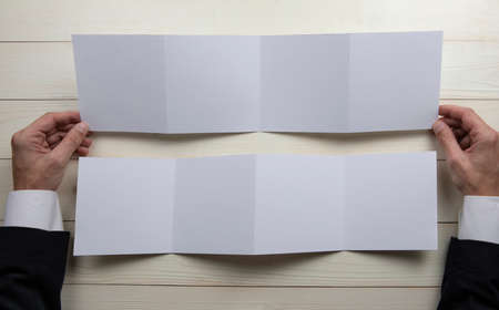Mens hands holding empty white booklet on wooden background. View from above