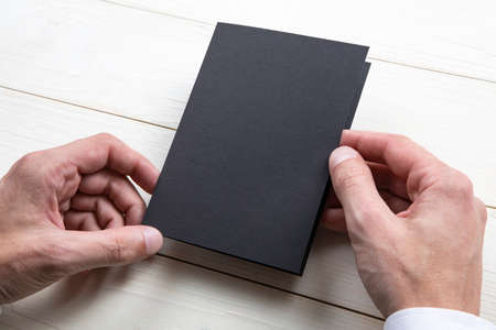 Mens hands holding empty black booklet on gray background. View from above