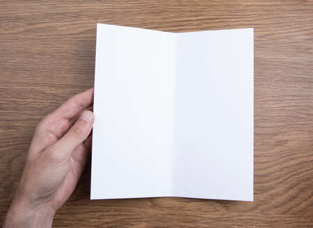 Mens hands holding empty white booklet on wooden background. View from above