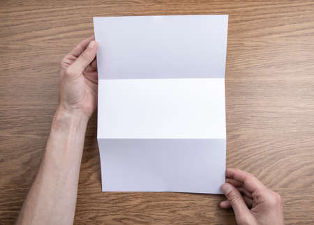 Mens hands holding empty white booklet on wooden background. View from aboveの写真素材